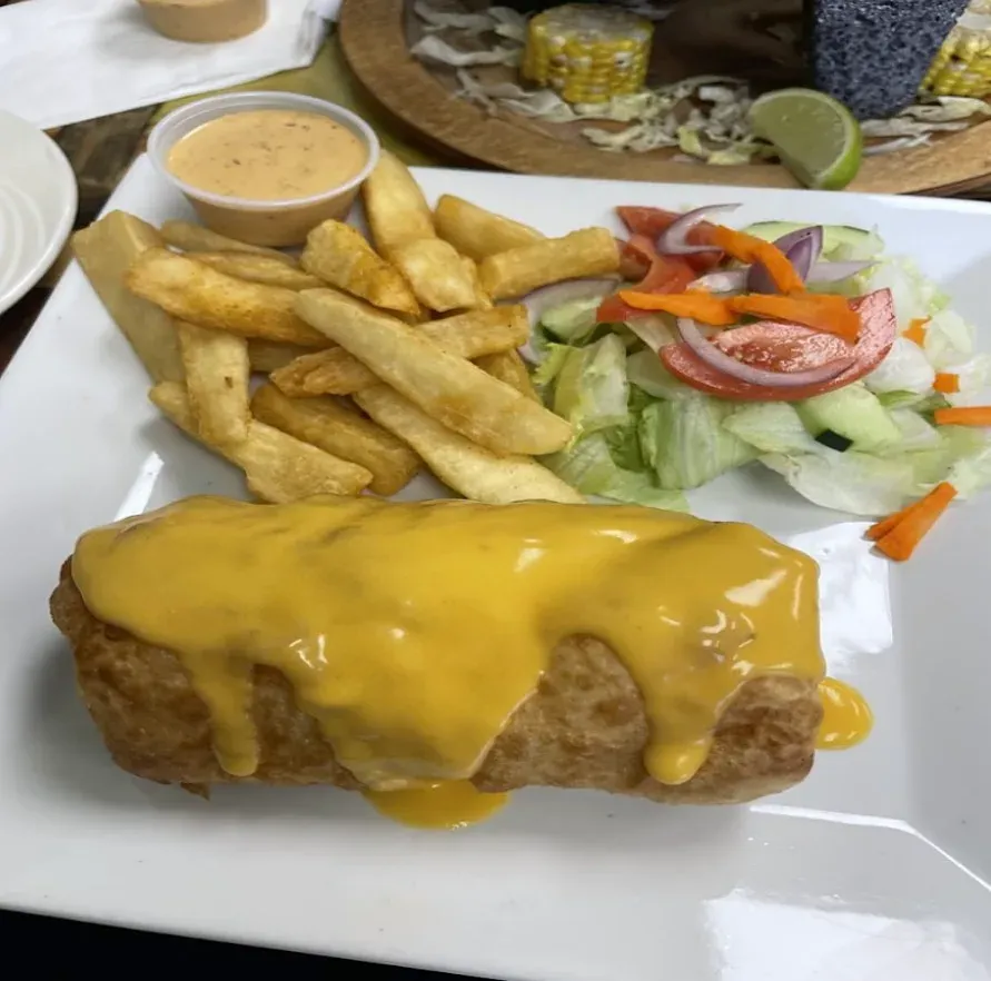 A chimichanga under melted cheese sauce with fries and a side salad