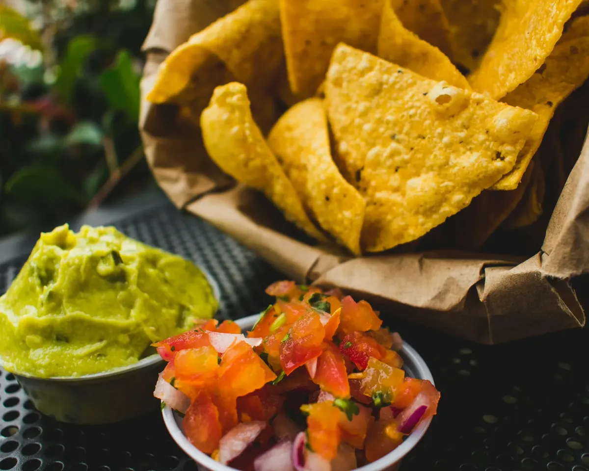 Tortilla chips in a paper-lined basket beside guacamole and pico de gallo