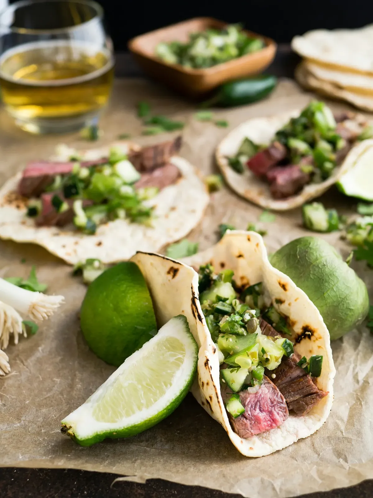 Steak tacos with chopped onion and cilantro on parchment with lime wedges