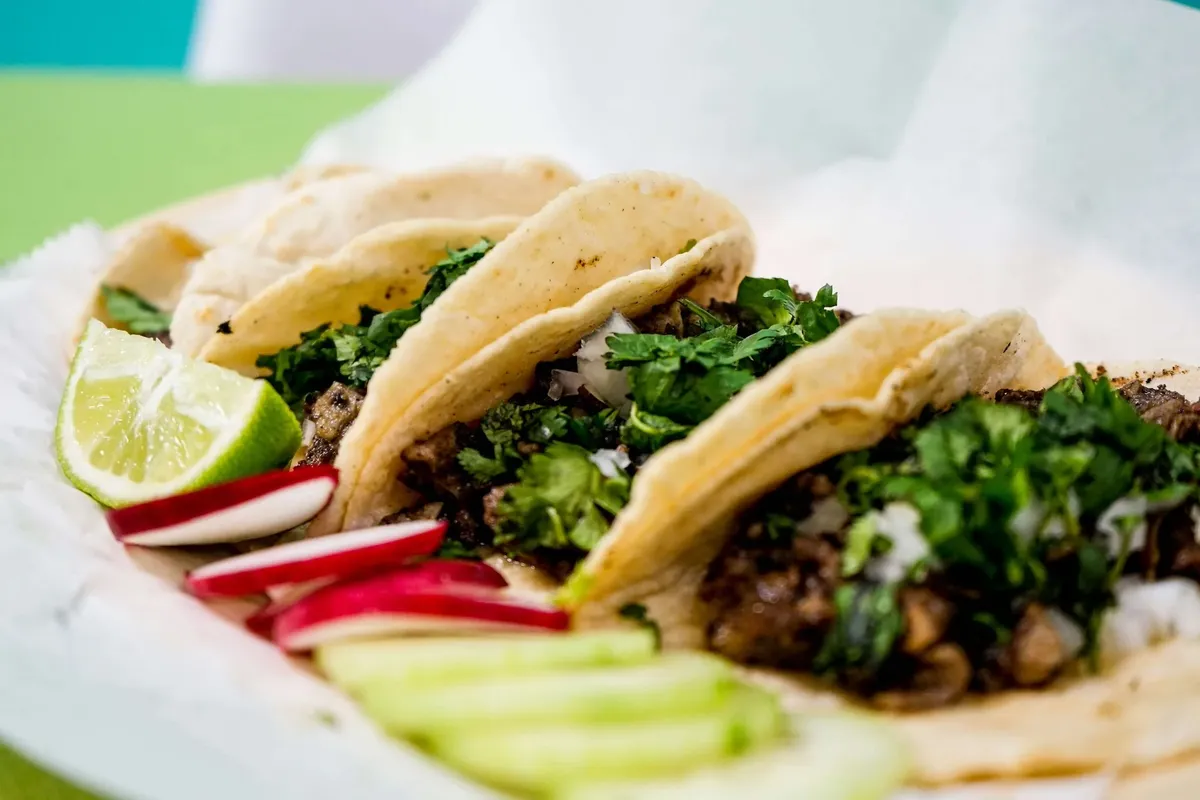 Three street-style tacos with cilantro, radish slices and a lime wedge