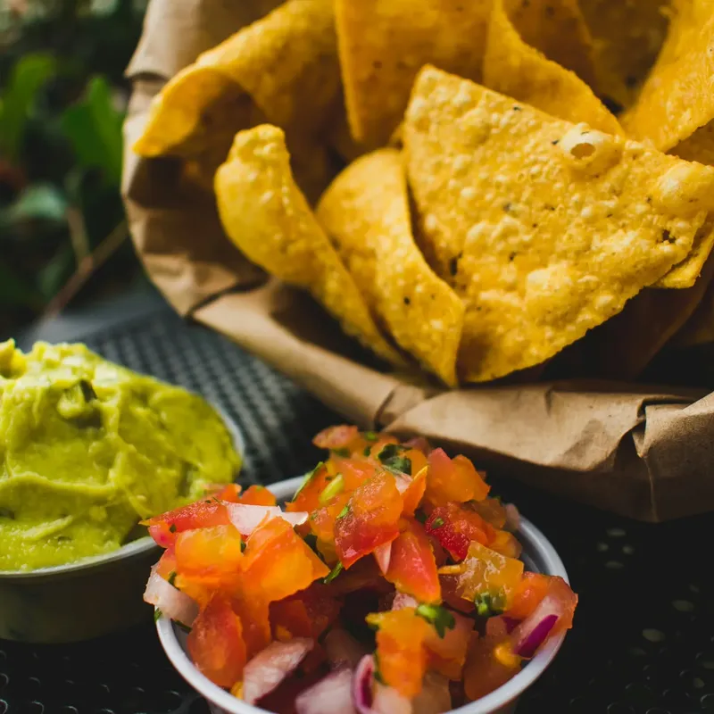 Tortilla chips in a paper-lined basket beside guacamole and pico de gallo