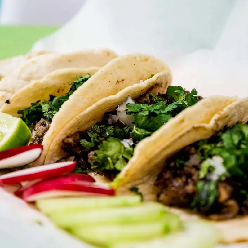 Three street-style tacos with cilantro, radish slices and a lime wedge